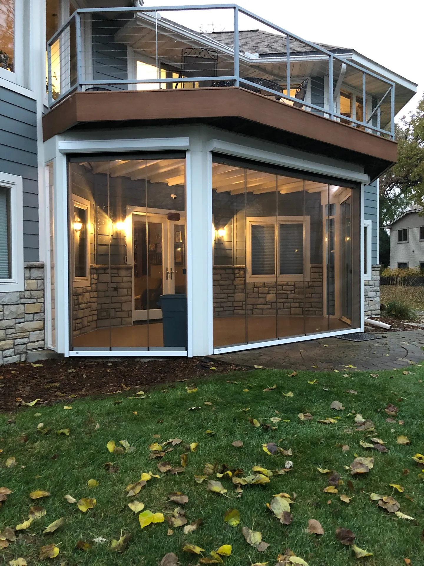 The same bay porch enclosed in frameless glass, warmly lit at dusk