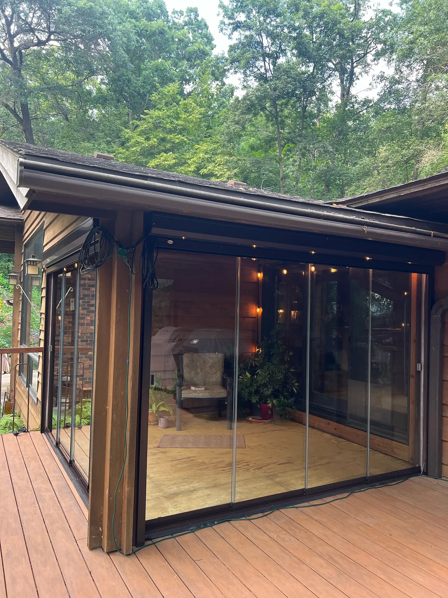 Wooded cabin porch enclosed in frameless glass with warm string lights