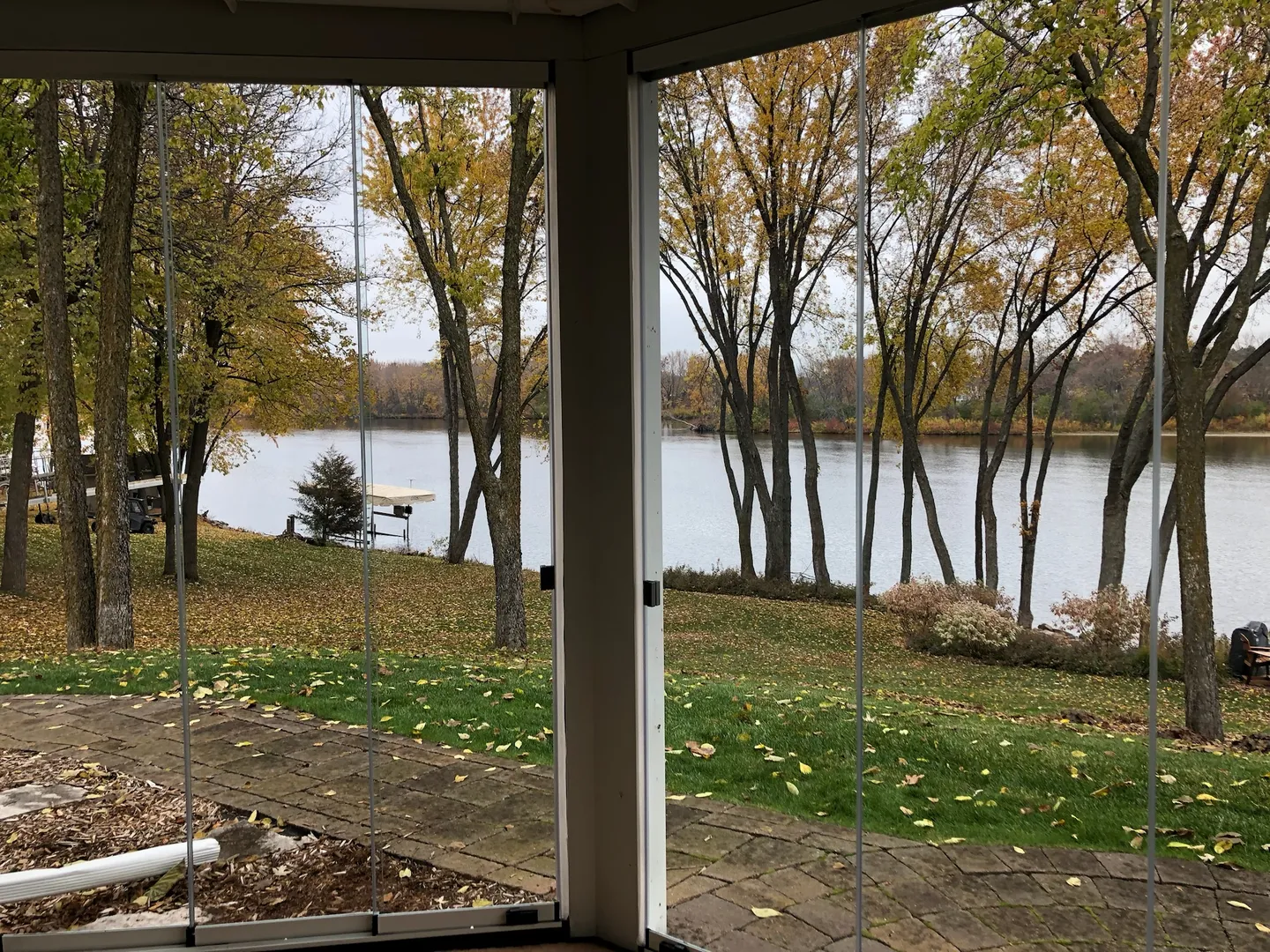 Golden October trees and a lake seen through frameless glass porch panels