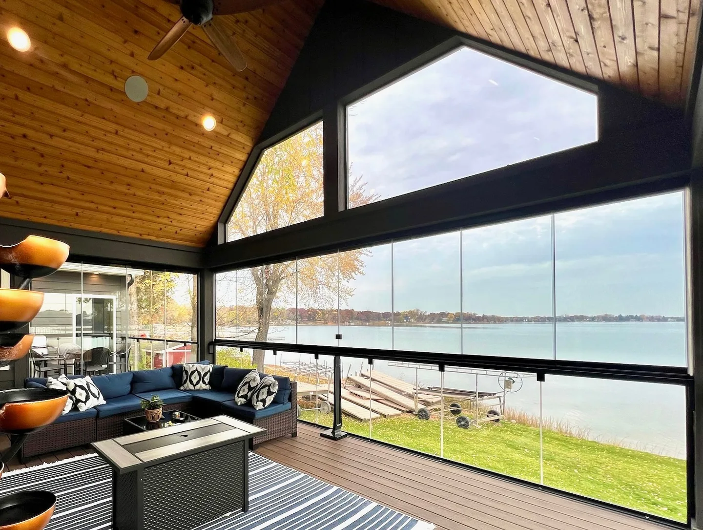 Wood-vaulted porch with a fire table, glass railings and open water beyond